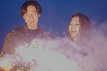 Young man and woman playing hand-held fireworks on the beach at nightの写真素材