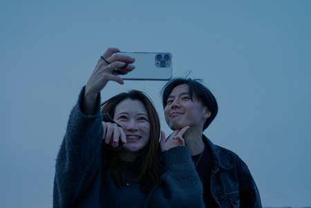Young man and woman taking photos on the beach just after sunsetの写真素材
