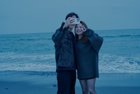 Young man and woman taking photos on the beach just after sunsetの写真素材