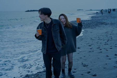 Young man and woman walking on the beach just after sunsetの写真素材