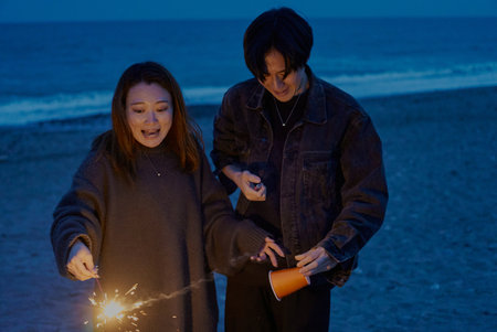 Young man and woman playing hand-held fireworks on the beach at nightの写真素材