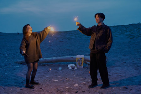 Young man and woman playing hand-held fireworks on the beach at night