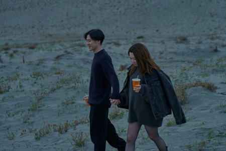 Young man and woman walking through sand dunes on a cloudy eveningの写真素材