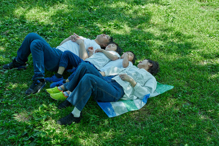 A family of four relaxing and snuggling together in a green space on a sunny day