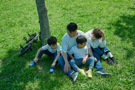 A family of four relaxing and snuggling together in a green space on a sunny day