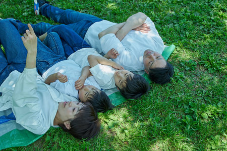 A family of four relaxing and snuggling together in a green space on a sunny day