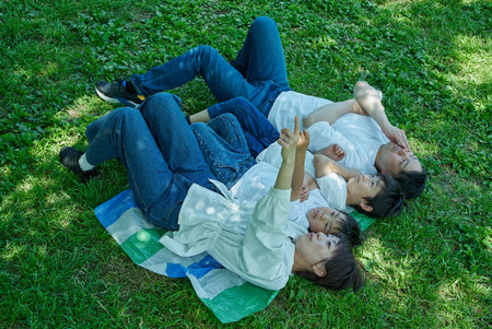 A family of four relaxing and snuggling together in a green space on a sunny day