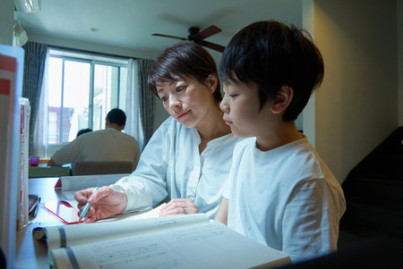 A boy studying in his room at home, watched by his mother