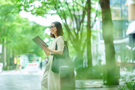 A young woman operating a tablet PC on a street cornerの写真素材