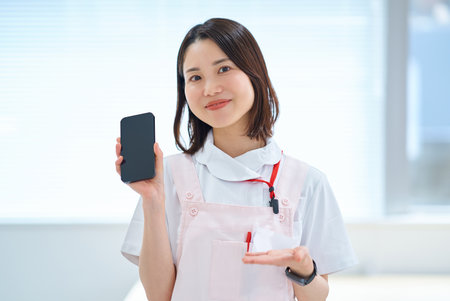 A woman in a white coat and apron holding a smartphoneの写真素材