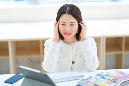 A woman looking tired while working on a computerの写真素材