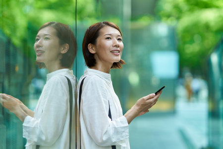 Asian woman holding a smartphone and waving in the streetの写真素材