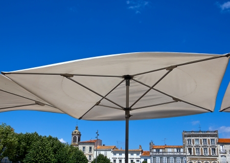 Big white terrace umbrella against blue sky and the buildings of Rochefort, Franceの写真素材