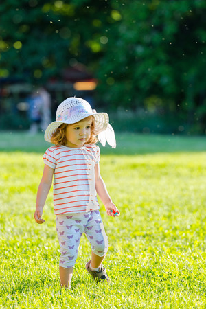 Cute little girl with fancy hat walking in the grass in summer timeの写真素材