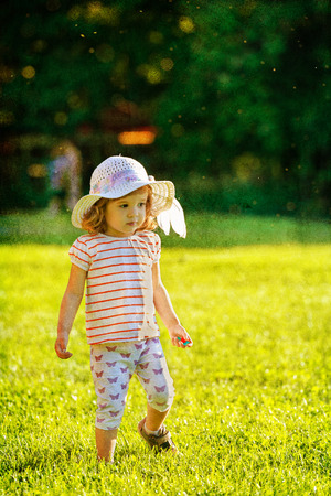 Cute little girl with fancy hat walking in the grass in summer timeの写真素材
