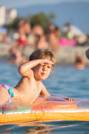 Cute little girl sitting on a floatable mattress, covering his eyes from the sunの写真素材