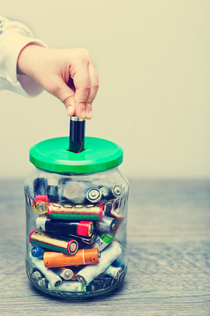Kid hand filling the jar with used AA and AAA batteriesの写真素材