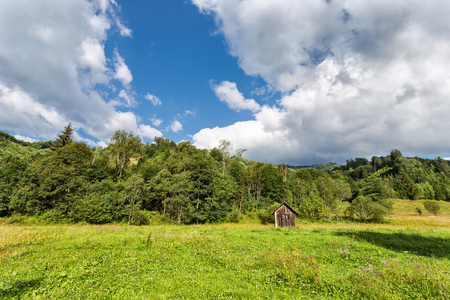 Mountain landscape with wooden shed and white clouds on blue skyの写真素材