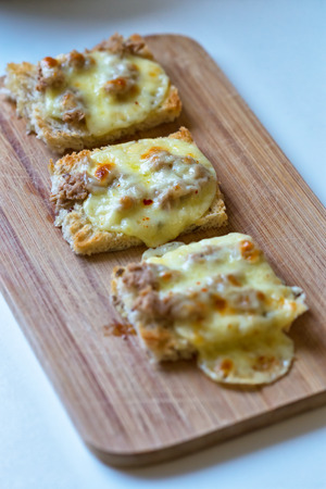 Three tartines of melted mozzarella and tuna flakes on a wooden plate for breakfastの写真素材