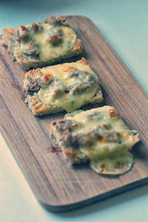Three tartines of melted mozzarella and tuna flakes on a wooden plate for breakfast - retro vintage filterの写真素材