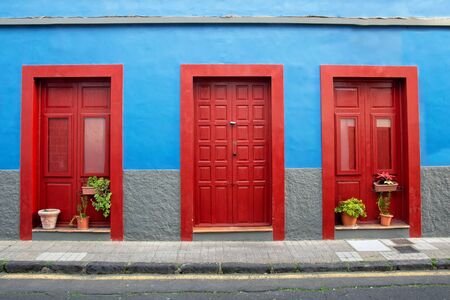 Red door on a background of blue walls in a Spanish town on the island of Tenerifeの写真素材