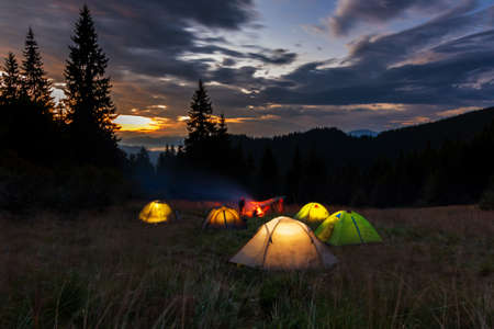 Evening in the Ukrainian Carpathians. Tents glowing on the lawn on a background of sunset. Camping in the mountains.の写真素材