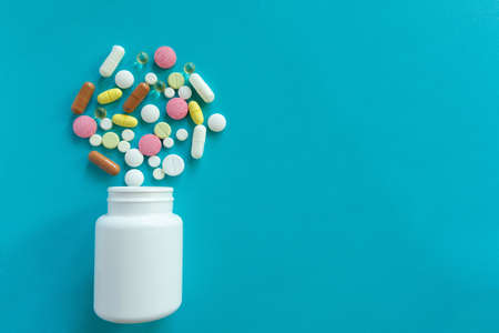 Many pills are poured from a medicine bottle. Pills and pills on a blue background. Medical tablets:...