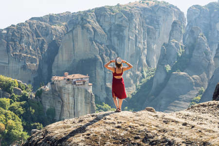 Young woman sits back to the camera on top of the mount and looks at the valley and rocks. Concept of travelling, happiness, freedom. Traveler enjoying the landscape from mountain, Meteora, Greeceの写真素材