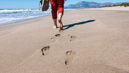 Footprints on the sand foot of a girl walking with sneakers in hand. Girl running with a dog on the Patara beach, Turkeyの写真素材