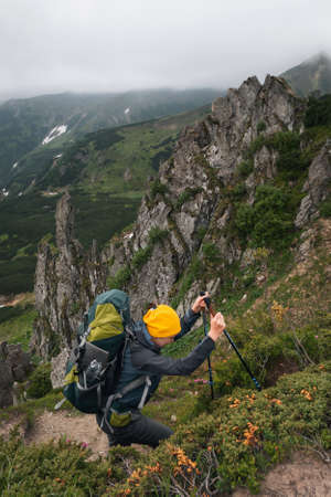 Girl hiker stands on a rock in the mountains. Trekking life. Hike through the Carpathian mountains. Green mountain slopes and blooming rhododendron.の写真素材