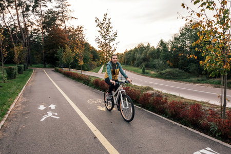Happy active woman riding bike bicycle in fall autumn park. Glad young girl in jacket and scarf relaxing. Healthy lifestyle and recreation leisure activity.の写真素材
