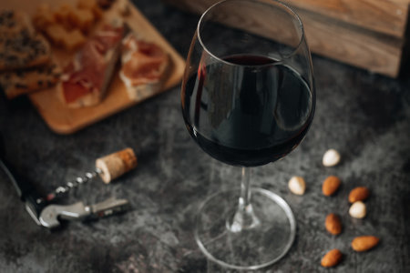 Red wine in glass. Glass of red wine are on the table. Prosciutto with cheese, red wine, baguette, nuts. Red wine with traditional Mediterranean snacks.の写真素材