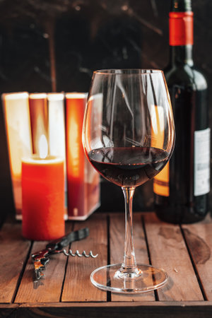 Red wine in glass. Glass of red wine are on the table. A candle, books and a bottle of wine on the table.の写真素材