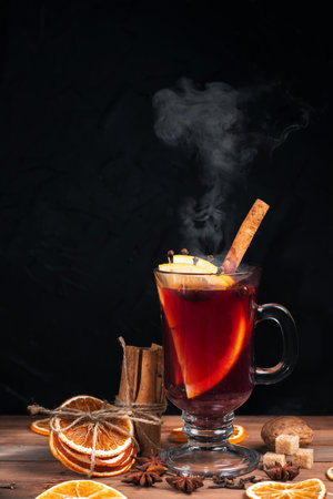 Glass of hot mulled wine stand on a dark background. A tray with ingredients for mulled wine - cinnamon, star anise, citrus fruits. Place for textの写真素材