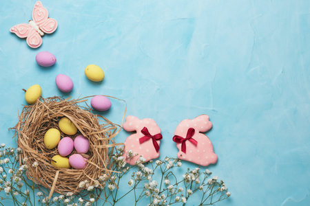 Banner for the Easter holiday. Colored eggs in a straw nest and white spring flowers on a blue...
