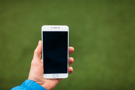 Man holding phone in hand, on a background of green soccer field. Black screen, you can insert text...