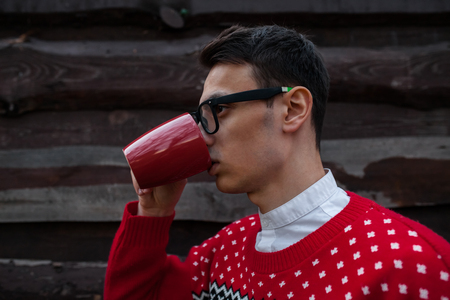 Portrait of a boy in a Christmas sweater drinking coffee, on a background of wooden wall. Isolated place for the photoの写真素材