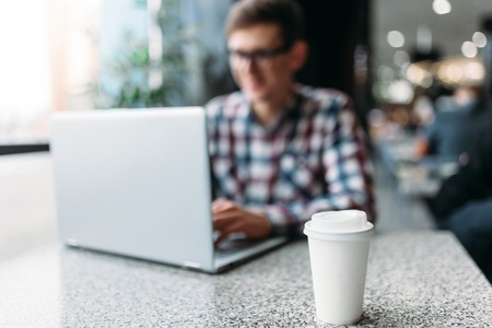 White paper Cup on the background of the working person, focus on the main subject, coffee or tea Cupの写真素材