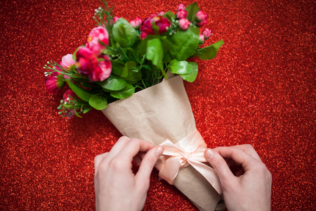 Valentine's day,florist woman packs a bouquet of flowers of roses in a paper wrapper with a bow on wooden table, suitable for advertisement, insert textの写真素材