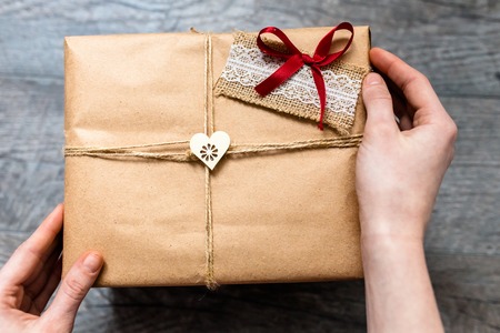 Female hand holding a wrapped gift ,Valentine's Day, romantic photo . Romantic grey wooden...