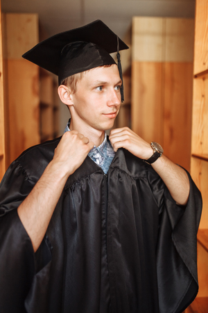 Successful graduate guy, in academic dresses, posing in the library, can be used for advertising,の写真素材