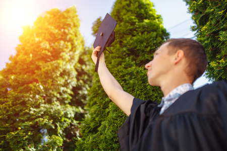 The successful graduate guy , in academic gowns, raised graduation cap, goodbye school , can be used for advertisement,の素材 [FY310103036008]