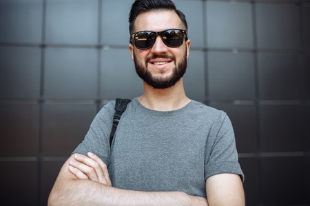 Portrait of a beautiful stylish guy, hipster with glasses, dressed in a gray empty t-shirt, standing...
