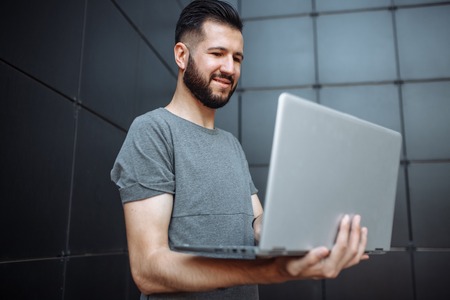 Portrait of handsome stylish guy, the hipster, working on laptop, wearing a gray blank t-shirt...