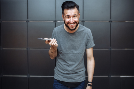 Emotional portrait of a stylish guy's guy, hipster, dressed in a gray blank t-shirt, standing in front of a black wall.の写真素材