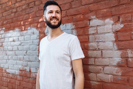 Portrait of a stylish and positive Guy, in a white empty t-shirt, against the orange brick wall,の写真素材