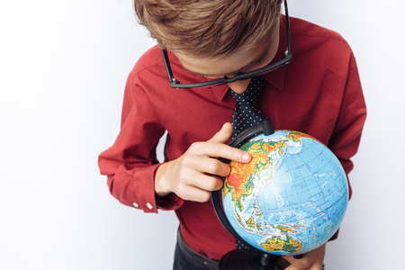 Portrait of positive and emotional schoolboy, with globe, white background, glasses, red shirt, business theme,の写真素材
