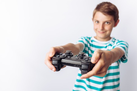 Portrait of a beautiful and emotional boy, in whose hands the game joystick, playing games, shows joy, white background, blue t-shirt,の写真素材