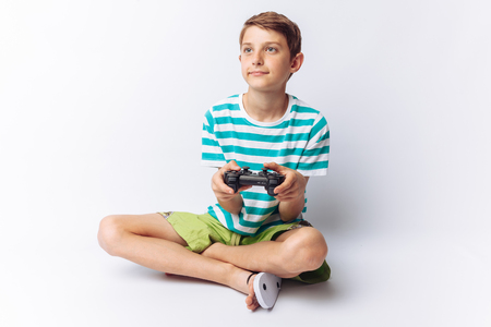Portrait of a beautiful and emotional boy, in whose hands the game joystick, playing games, shows joy, white background, blue t-shirt,の写真素材