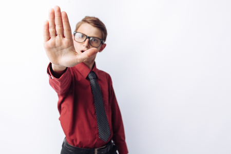 Portrait of positive and emotional schoolboy, posing and showing stop hand, white background, glasses, red shirt, business theme,の写真素材